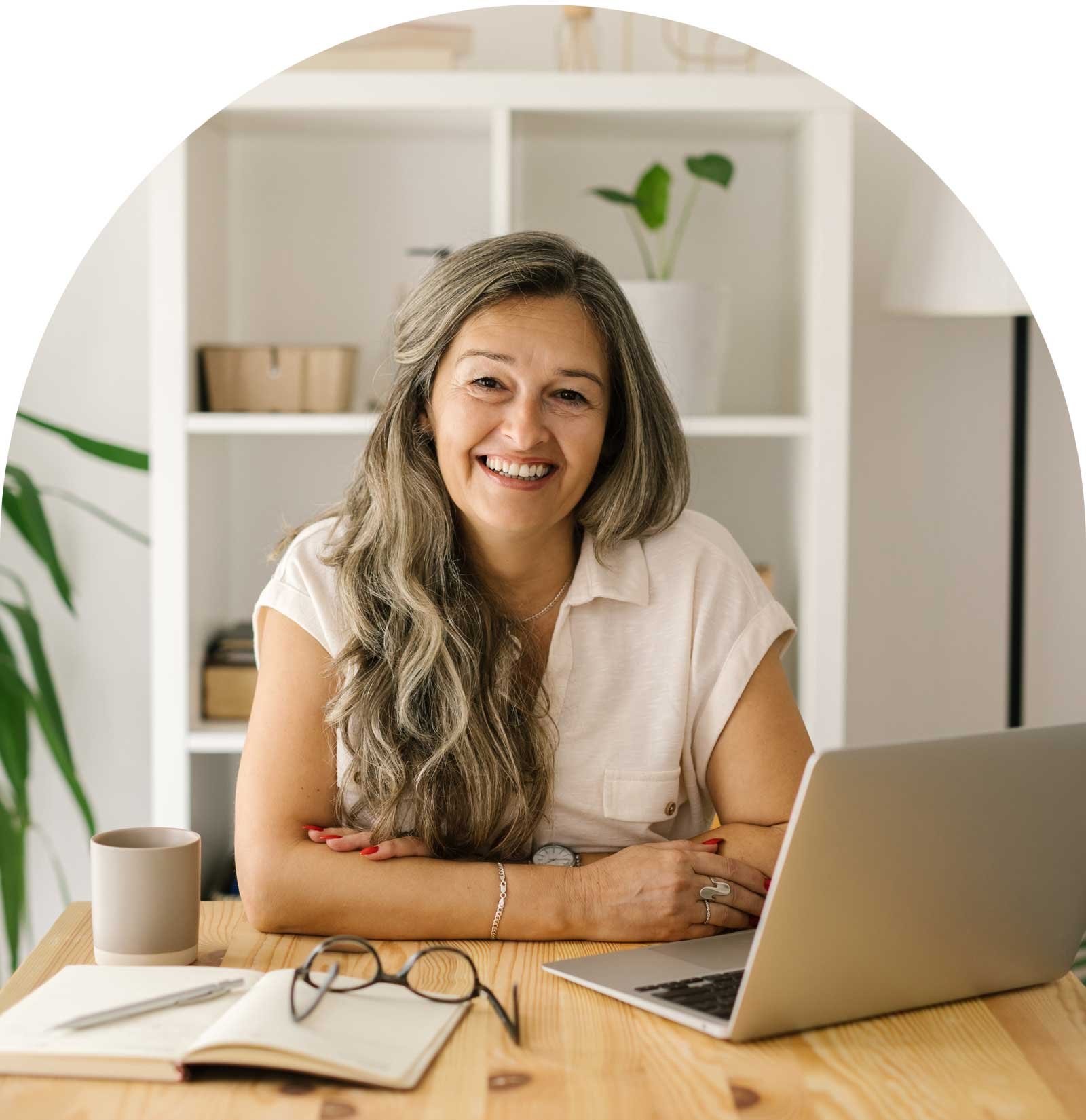 Woman sitting at desk smiling with laptop